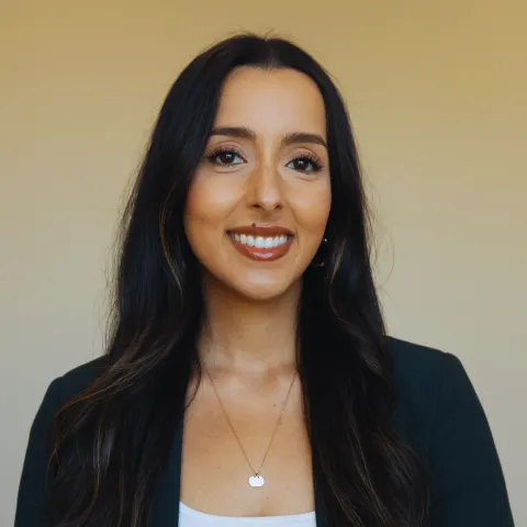 A smiling woman with long, dark hair wearing a blazer.